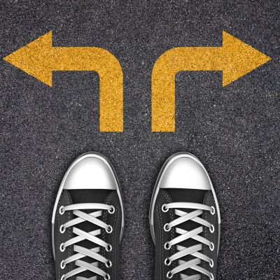 A person standing at a crossroads with arrows pointing in two different directions, representing choices.